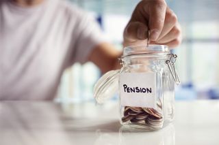 Foto: Person wirft Münzen in Glas mit Aufschrift Pension